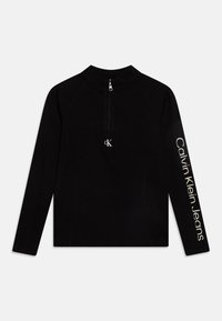 Black long-sleeve top with a high collar and half-zip. Features ribbed texture and white "Calvin Klein Jeans" text down the left arm.