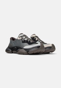 Scarpe da ginnastica grigie e nere con una tomaia testurizzata, punta arrotondata, suola spessa e dettagli a contrasto. Materiali resistenti con chiusura a lacci.