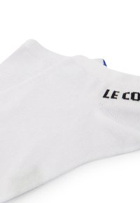 Calcetines de algodón blancos con un corte corto, acento azul en el talón y el nombre de la marca "LE COQ" en negro en el puño acanalado.