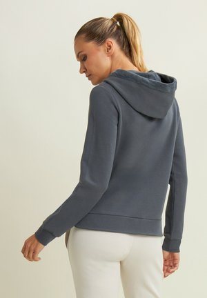 Sweat-shirt à capuche gris avec une texture douce, des manches ajustées et une poche kangourou. Le dos présente une coupe décontractée et des coutures subtiles.