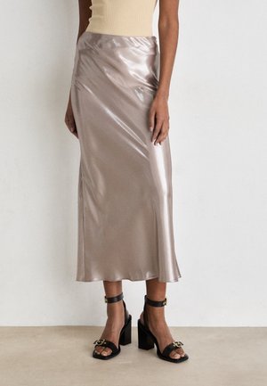 Kvinde iført en skinnende sølvfarvet satin midi nederdel med sorte høje hæle sandaler med ankelstropper og spænde detaljer.