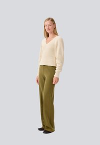 Beiger V-Ausschnitt Strickpullover mit gerippter Textur, kombiniert mit hochtaillierten olivgrünen Hosen und schwarzen Ballerinas. Einfaches, lässiges Outfit.