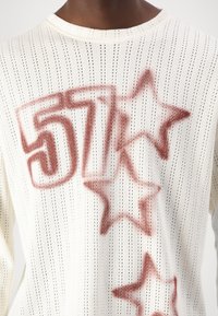 Maglione bianco lavorato a maglia con un motivo perforato, caratterizzato da testo sprayato rosso "57" e design a stella. Collo rotondo e vestibilità ampia.