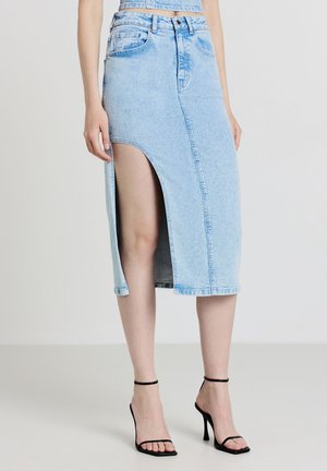 Jupe en denim bleu clair avec une fente devant, ourlet brut et design classique à cinq poches. Associée à des sandales à talons hauts noires à lanières.