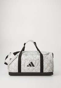 Bolsa de deporte con un patrón geométrico gris, base negra y bolsillo lateral de malla. Cuenta con dos asas negras y un cierre con cremallera.