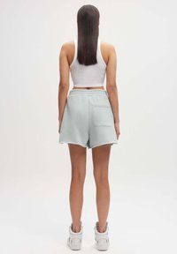 Lichtblauwe katoenen shorts met een relaxed fit, voorzien van een achterzak, een elastische tailleband en rafelige details aan de zoom. Draagt met witte sneakers.