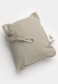 Cuscino beige con superficie testurizzata, dotato di una cinghia per il trasporto e di un moschettone silver. Forma distintiva a orecchie di gatto con etichetta del logo.
