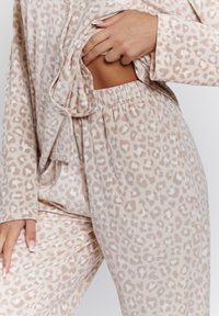 Conjunto de lounge de estampado de leopardo en tela suave, que incluye una parte superior abotonada y pantalones con cinturilla elástica, en tonos neutros de beige y crema.