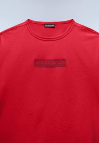 Κόκκινο βαμβακερό t-shirt με στρογγυλή λαιμόκοψη και ανάγλυφο ορθογώνιο ετικέτα με το λογότυπο "Napapijri geographic" στο μπροστινό μέρος.