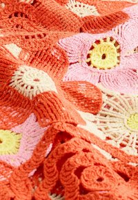 Krosettu peitto, joka esittelee eloisia oransseja, vaaleanpunaisia ja keltaisia kukkakuvioita, joissa on teksturoituja ompeleita ja monimutkaisia yksityiskohtia.