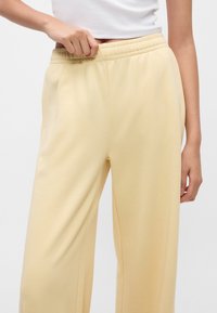 Κίτρινες φόρμες από μαλακό ύφασμα με ελαστική μέση και πλευρικές τσέπες, με χαλαρή εφαρμογή και λεία υφή.