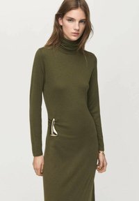 Vestido de cuello alto color verde oliva con mangas largas, corte ajustado y un detalle metálico en contraste en el lateral, confeccionado con tela de punto suave.