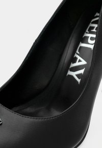 Μαύρο γυναικείο παπούτσι με ψηλό τακούνι από λείο δέρμα, με στρογγυλεμένη μύτη, που διαθέτει διακριτική γυαλάδα στην επιφάνεια και λογότυπο εκτυπωμένο στην εσωτερική σόλα.