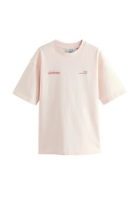 Camiseta de algodón de manga corta en rosa claro. Presenta un cuello redondo, un ajuste relajado y texto impreso en rojo y negro en la parte frontal.