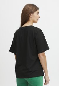 Sort bomulds T-shirt med en afslappet pasform, faldende skuldre og korte ærmer, set fra ryggen mod en ensfarvet hvid baggrund.