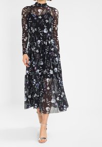 Robe noire à motifs floraux avec de longues manches transparentes, corsage ajusté et jupe fluide. Présente un motif floral vibrant en violet, blanc et vert.