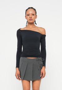 Crna dugazna majica s dizajnom bez rukava i nabranom teksturom, uparen s plisiranom sivom suknjom koja ima detalj vezivanja sa strane.