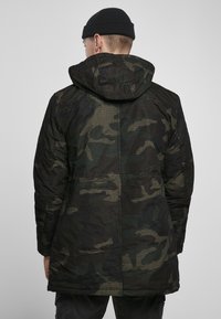 Parka jakna s kamuflažnim vzorcem v črnih in zelenih odtenkih, ki ima kapuco, qiltan dizajn in teksturirano tkanino.