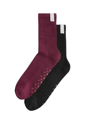 Pair of ribbed crew socks, one burgundy and one black, each with heart-shaped non-slip grips on the sole and a white fabric tag near the cuff.
