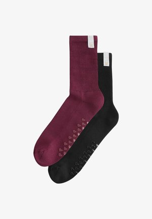 Pair of ribbed crew socks, one burgundy and one black, each with heart-shaped non-slip grips on the sole and a white fabric tag near the cuff.