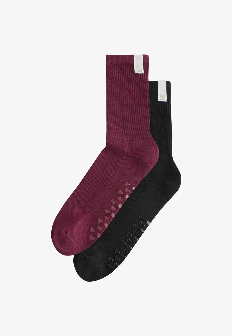 Pair of ribbed crew socks, one burgundy and one black, each with heart-shaped non-slip grips on the sole and a white fabric tag near the cuff.