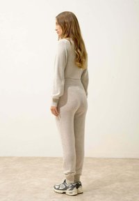 Ljust grått stickat loungewear-set med en figurnära silhuett, ribbade muddar och matchande joggerbyxor, som bärs med grå sneakers.