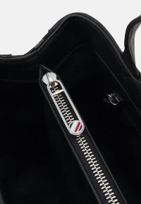 Interno di una borsa in pelle nera che presenta una cerniera in metallo argentato con una pratica linguetta rotonda, tessuto con motivo e una texture simile alla scamosciata.