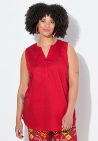 Top rosso senza maniche con scollatura a V e dettagli plissettati, realizzato in tessuto morbido. Abbinato a pantaloni colorati e stampati con disegni geometrici.