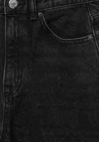 Gros plan sur un jean en denim noir montrant la poche avant, la boucle de ceinture, les coutures et les rivets métalliques sur un tissu texturé.