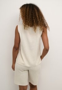 Beige ärmlös topp och matchande shorts i texturerad tyg, med en avslappnad passform och fålldetaljer. Modell sedd bakifrån.
