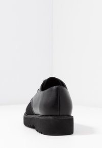 Chaussure en cuir noir avec un panneau en tissu noir texturé, bout arrondi et une semelle en caoutchouc noir robuste avec un motif à relief.