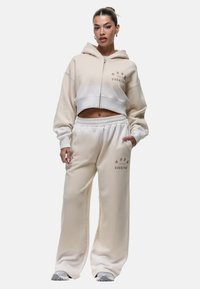 Lichtbeige cropped hoodie met een rits en logo, gecombineerd met een losse, bijpassende sweatpants met een elastische tailleband.