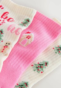 Trei șosete festive cu modele de Crăciun: albă cu om de turtă dulce și brad, roz cu casă de turtă dulce și albă cu mai multe brazi de Crăciun.
