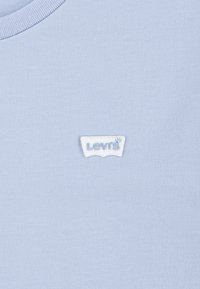 Šviesiai mėlynas medvilninis marškinėliai su banguotu apvaliu kaklu ir balta išsiuvinėta „Levi's“ logotipo etikete ant krūtinės. Minkšta, lygi tekstūra.