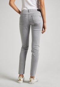 Vaqueros de mezclilla gris ajustados con un ligero desgaste, dos bolsillos traseros y un ligero estiramiento para mayor comodidad, combinados con zapatillas con detalles en plateado.