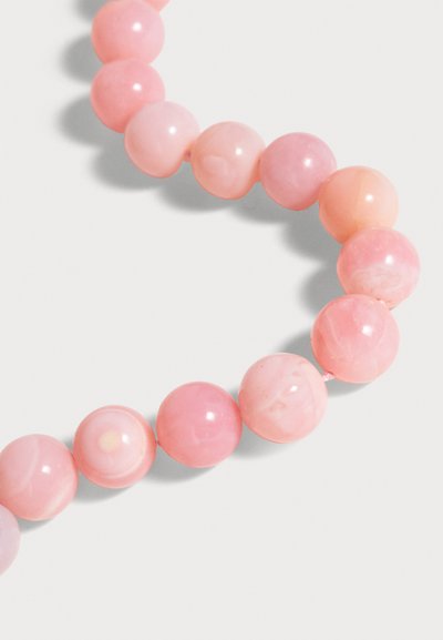 Gros plan d’un collier avec des perles rondes et lisses roses sur fond blanc, disposées en ligne courbe.