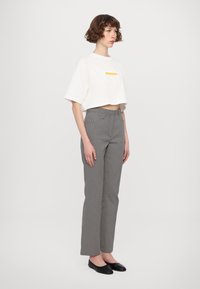 T-shirt blanc court avec des accents jaunes, associé à un pantalon taille haute noir et blanc à motifs losange. Le modèle porte des ballerines noires.