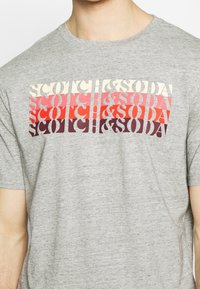 Grå bomulds t-shirt med et stiliseret flerfarvet grafik med teksten "SCOTCH & SODA." Kort ærmer, rund halsudskæring, afslappet pasform.