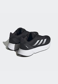 Scarpe sportive nere con una parte superiore in tessuto a rete traspirante, suola intermedia bianca e un design a tre strisce argentate; presentano un tallone rinforzato e dettagli testurizzati.