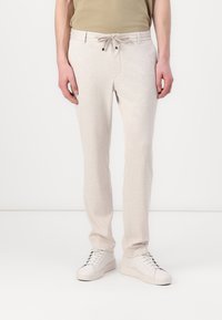 Hellgraue, zulaufende Jogginghosen mit einem Kordelzugbund und seitlichen Taschen, aus weichem Stoff. Kombiniert mit weißen Sneakers.