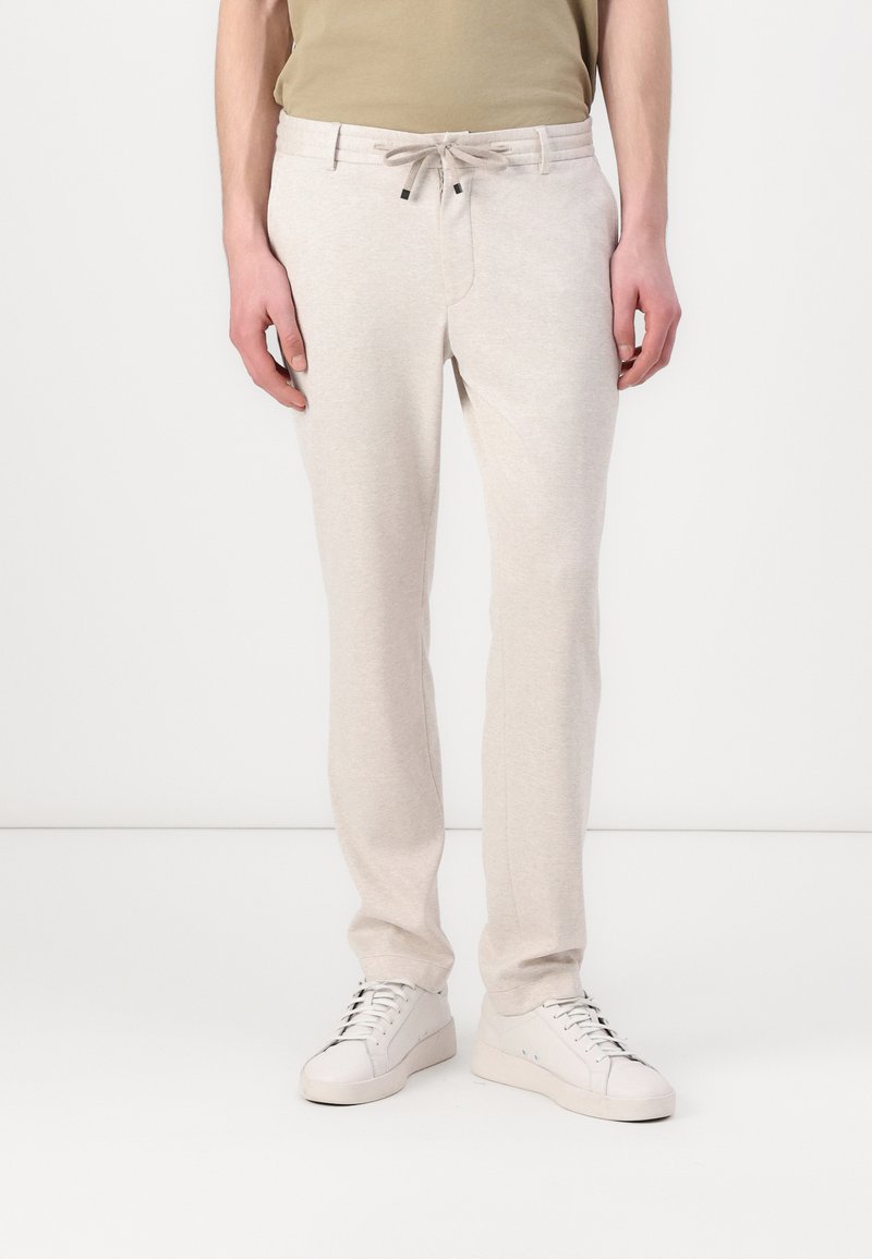 Hellgraue, zulaufende Jogginghosen mit einem Kordelzugbund und seitlichen Taschen, aus weichem Stoff. Kombiniert mit weißen Sneakers.