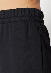 Svarta bomulls-sweatpants med ribbad elastisk midja och sidofickor, som visar en slät textur och avslappnad passform.