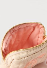 Μικρό μπεζ ραμμένο πουγκί με χρυστό φερμουάρ, ανοικτό για να δείξει το εσωτερικό επένδυσης από απαλό ροζ ύφασμα.