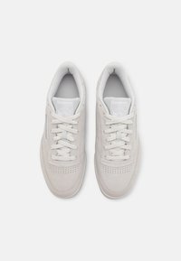 Zapatillas Reebok de color gris claro con parte superior de ante, puntera perforada, cordones planos y collar acolchado. Presenta un logo en la lengüeta y suela lisa.