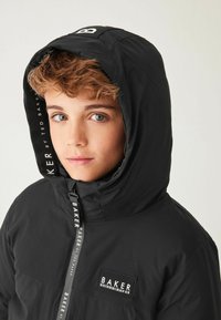 Veste à capuche noire avec fermeture éclair à l'avant, arborant le logo "BAKER" sur la capuche et la poitrine. Matériau léger avec une texture lisse.