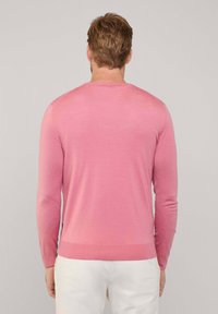 Suéter de punto de color rosa claro con mangas largas y cuello redondo. Presenta puños y dobladillo acanalados. Textura suave, diseño minimalista.