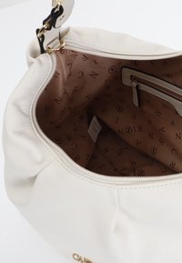 Valkoinen nahkalaukku pehmeällä, rypytetyllä muotoilulla. Sisäpuolella on beige vuori, jossa on toistuva brändäys ja vetoketjullinen tasku. Kultaista metalliosaa.