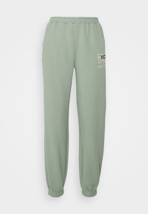 Lichtgroene joggingbroek met elastische taille, omgeslagen enkels en een klein crème-zwart logotekstje op de bovenste linker dij.