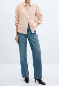 Chemise en lin pêche clair avec fermeture à boutons, associée à un jean bleu taille haute. Des bottines noires ajustées à talons complètent la tenue.