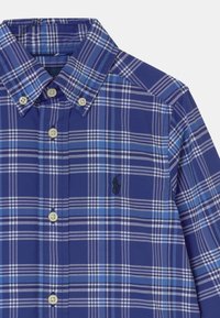 Modrá károvaná košile na knoflíky s krátkým límečkem, s bílými a světle modrými pruhy, plastovými knoflíky a malým černým vyšívaným logem.